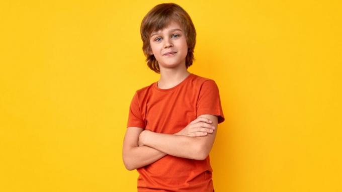 Positiv preteen gutt i uformelt antrekk som holder armene krysset og ser på kameraet mot levende gul bakgrunn